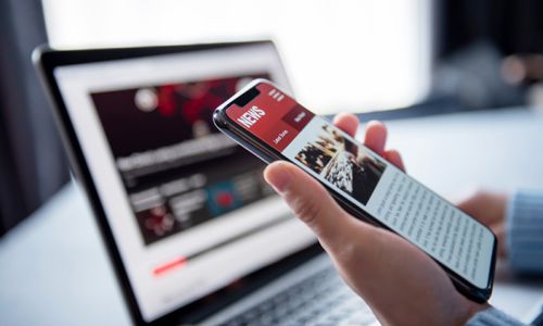 Online news on a smartphone and laptop. (Mockup website). Woman reading news or articles in a mobile phone screen application at home. Newspaper and portal on internet, copy space.