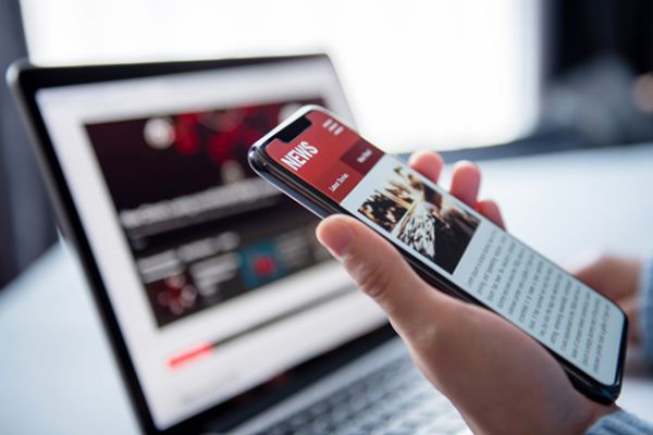 Online news on a smartphone and laptop. (Mockup website). Woman reading news or articles in a mobile phone screen application at home. Newspaper and portal on internet, copy space.